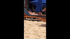 Topless sunbather using tweezers to pluck hairs from her armpit on beach in Bali