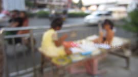 Thai kids on a table by the side of a busy Bangkok street, doing their school homework