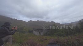 Harry Potter Train crosses over the Glenfinnan Viaduct, Scotland being filmed by a man using his mobile on a rainy day. 