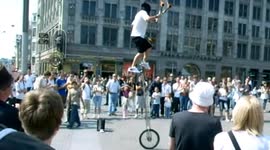 Blindfolded man juggles with flaming clubs on tall unicycle