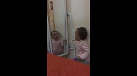 The two years old girl talking with herself in the mirror
