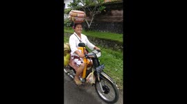 Motorcycling supermum in Bali carries groceries on her head and 4 gas cylinders