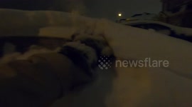 man brushing snow off of car after snowstorm