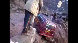 Car desperately tries to drive out of mud on precarious mountain road