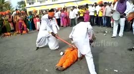 Blindfolded man wielding axe cracks open coconuts balanced on women