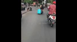 Tourist drags suitcase alongside motorcycle taxi by its wheels