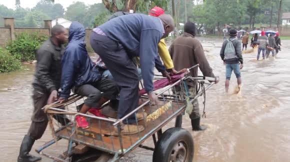 Pedestrians pay 10p to be taken across fast moving flood waters in Kenya