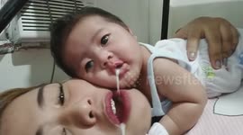 Yuk! Baby throws up in sister's mouth as they lay on bed together in Philippines