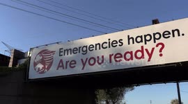Sign near Toronto in Markham at railway crossing warning people to be prepared in case of any emergency as a train rumbles over the bridge with freight and tanker cars