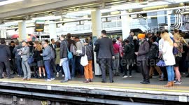 A teenage girl in a Hogwarts skirt leans forward near the tracks to see past a stranger, and tries to get a peak on an upcoming train