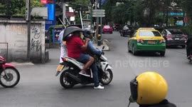 Thai man holds chair on head while sitting at back of motorcycle