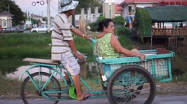 Caring husband transports his wife by pedal power on a tricycle.