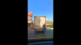 Teenager Sits On Bumper Of Moving Truck Playing Phone