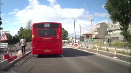 Man walks out from behind one bus in front of a learner then runs out in front of another from the opposite side making them to stop abruptly