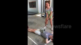 Girl uses big hammer to smash a concrete block resting on her friends stomach