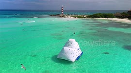 Aerial Drone footage over people playing in the Caribbean Sea with a lighthouse in the background