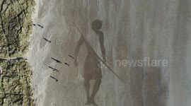 Artist creates incredible 150ft sketch of giant surfer on UK beach using garden RAKE