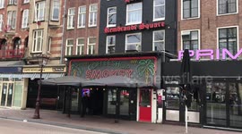 Amsterdam parent on transport bike with children passes closed coffeeshop on Rembrandt square