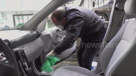 A man in a protective uniform disinfects his car to protect himself from the coronavirus