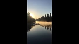 Two canoeists paddle into golden mist on the river Thames at sunrise in mesmeric footage
