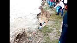 Lucky escape as man slips into raging floodwaters when riverbank collapses