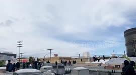 Rooftop and aerial view of George Floyd Protestors on the roof looking down on 3rd Street Los Angeles at the protestors facing the police with a pan to a helicopter flying over the rally