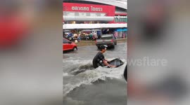 Thai man rides knee-boarding on flooded road after heavy rain