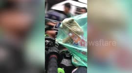 Puppy shelters in owner's raincoat while riding on motorcycle in Thailand