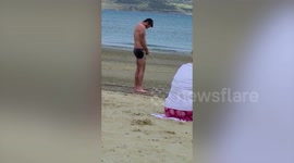 Drunk man urinates on a busy beach in front of shocked onlookers
