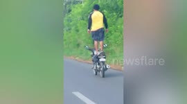 Daredevil motorcycle rider stands on seat while travelling along road in Philippines