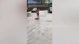 Thai man skimboards down road submerged by floodwater