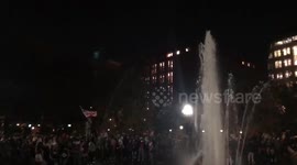 Man waves flag above crowd at Washington Square Park Fountain