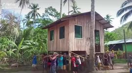 Filipino villagers help someone move home by picking the whole house up