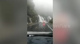 Dramatic moment drivers pass by water cascading down mountainside