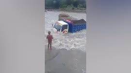 Delivery trucks make dangerous crossing of swollen river after heavy rain in Indonesia