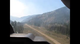 Light aircraft makes low bank over mountain treetops to land on riverside wilderness airstrip