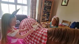 Two little princesses have tea party on their pony's back in a living room in England