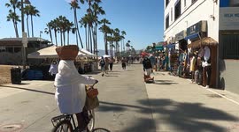 Woman Balancing Basket Riding Bicycle Down Venice Beach Boardwalk In LA, CA, US