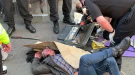 Police work to free the arms of two Extinction Rebellion protesters who have cemented their arms into a metal pipe