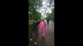 Man in bright pink suit arrives with his bicycle at Speakers Corner, London.  Man filming greets him as 'Mr Bertie Bassett'