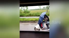 Woman rides scooter with umbrella blocking her view to shield herself from rain in China