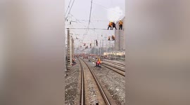 In China, railway workers hang from overhead cables to get the job done