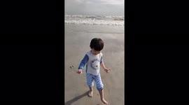 Funny video of a toddler falls down when running away from sea waves