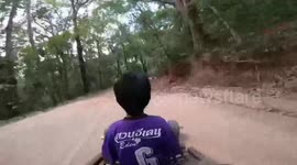 Boy excitedly rides wooden go-kart with tourist down a mountain