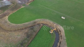 Aerial footage of a digger dredging a small river, showing satisfying progress as it clears reeds