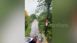 Motorcycle drives through wet narrow road with no guardrails