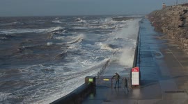 Elderly couple get wet and too close to the dangerous sea conditions along the sea wall in Blackpool UK