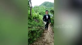Newly-wed couple giggle while walking together on muddy road to reach wedding reception