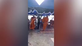 Buddhist monks hold up tent being battered by heavy rain