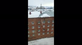 The woman calmly walked next to a block of snow falling from the roof